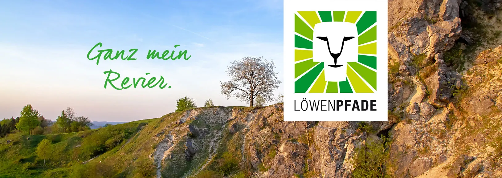 Löwenpfade – Ganz mein Revier: Naturerlebnis und Freiheit in der Löwenpfade-Region Landschaft mit grünen Hügeln, einem einsamen Baum und einem schmalen Pfad. Im Vordergrund das Logo von Löwenpfade: ein stilisierter Löwenkopf in grün-gelb-weißen Streifen mit dem Schriftzug LÖWENPFADE. Dazu der Slogan: Ganz mein Revier.